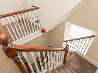 A staircase with brown carpet and white spindles with wooden handrails at Jubilee House in Embleton