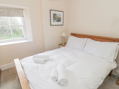 A bedroom with a double bed with white linens towels on the bed a bedside table with a lamp a window with patterned blind and a framed picture on the wall at Jubilee House in Embleton
