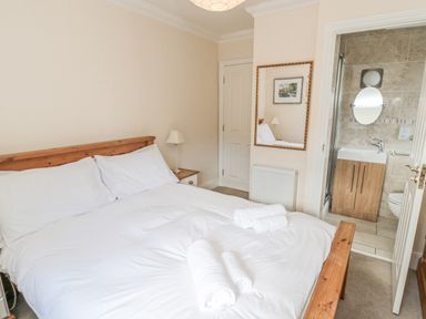 A bedroom with a double bed white linens bedside tables a mirror and an ensuite bathroom at Jubilee House in Embleton
