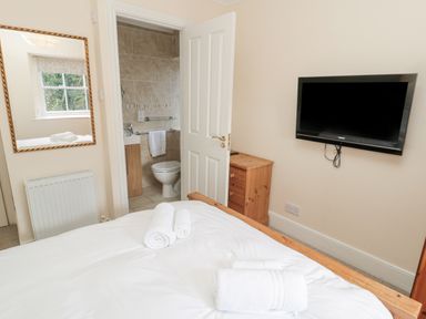 A bedroom with a bed and rolled towels a wall mounted television a wooden dresser a mirror and an open door revealing a bathroom at Jubilee House in Embleton