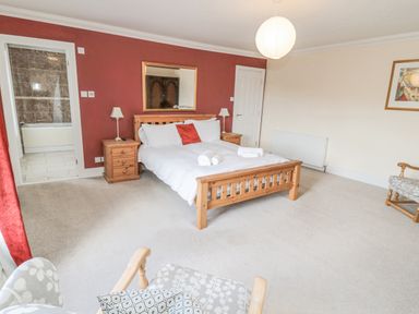 A bedroom with a wooden bed and nightstands and an armchair at Jubilee House in Embleton