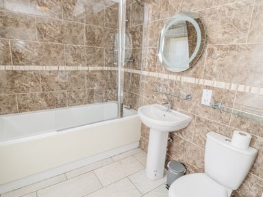 A bathroom with a bathtub shower combination a pedestal sink a toilet and a round mirror at Jubilee House in Embleton
