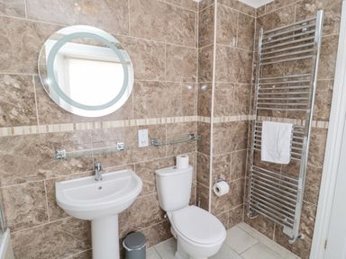 A bathroom with a sink and toilet with brown tiled walls at Jubilee House in Embleton