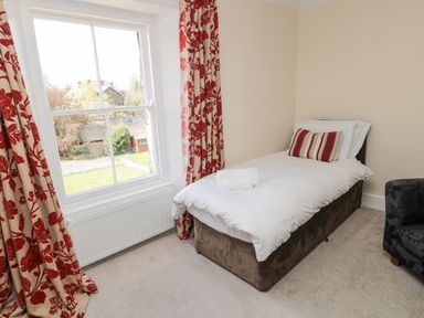 A bedroom with a single bed with white bedding and a striped pillow next to a window with floral curtains at Jubilee House in Embleton