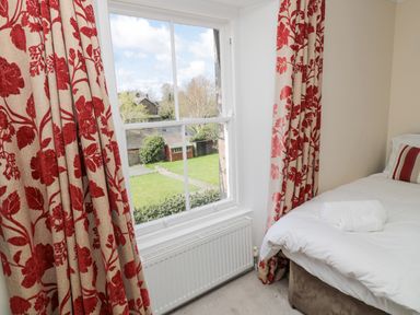 A bedroom with a bed near a window with red floral curtains and a view of a garden at Jubilee House in Embleton