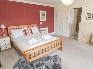 A bedroom with a wooden bed with white bedding and towels a dresser and a chair at Jubilee House in Embleton