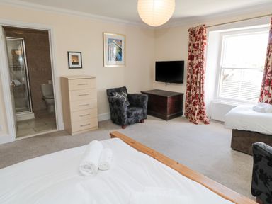 A bedroom with two beds rolled towels armchair chest tv dresser and window with floral curtains at Jubilee House in Embleton