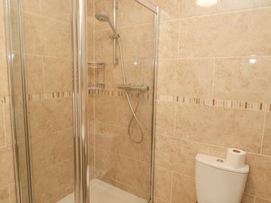 A shower area with glass doors and a toilet with a roll of toilet paper on top at Jubilee House in Embleton