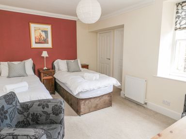 A bedroom with two single beds a bedside table a chair and a window at Jubilee House in Embleton