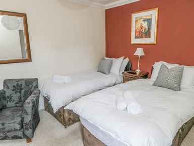 A bedroom with two beds a bedside table with a lamp a patterned armchair and a wall mirror at Jubilee House in Embleton