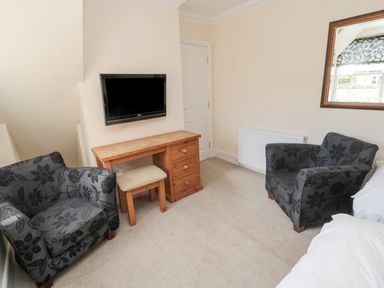 A sitting area with two armchairs a wooden desk and a wall-mounted TV at Jubilee House in Embleton