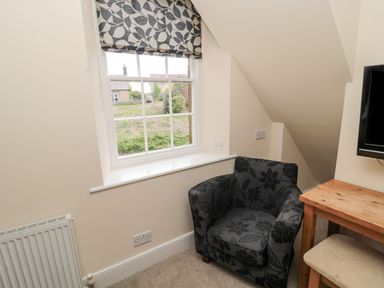 A room corner with a window and floral patterned armchair next to a wooden table and a mounted television at Jubilee House in Embleton