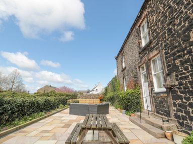 A stone patio with wooden picnic table and outdoor seating beside a stone building at Jubilee House in Embleton