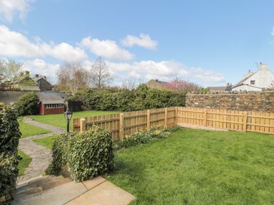 A garden with a stone path shrubs a wooden fence and a small shed at Jubilee House in Embleton