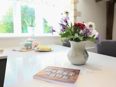 A kitchen countertop with a guest book a vase of flowers and a tray with cups and scones at Washpool in Milton-Under-Wychwood