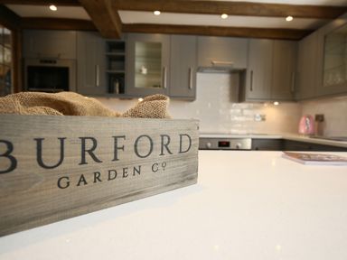 A kitchen with grey cabinets wooden beams and a wooden box on a white countertop at Washpool in Milton-Under-Wychwood