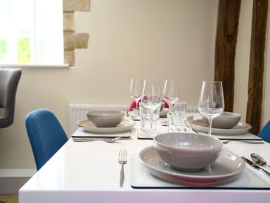 A dining table set with bowls plates cutlery and glasses with blue and gray chairs near a window at Washpool in Milton-Under-Wychwood
