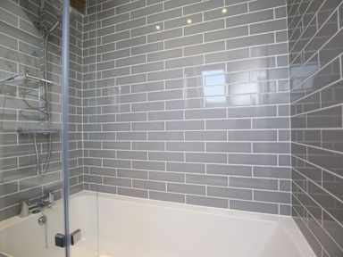 A bathroom with a white bathtub gray subway tile walls and a showerhead with glass shower screen at Washpool in Milton-Under-Wychwood