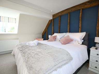 A bedroom with a large bed white bedding and pink pillows against a blue accent wall with wooden beams at Washpool in Milton-Under-Wychwood