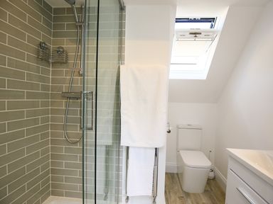 A bathroom with a glass shower enclosure and tiled walls a white toilet a towel rack with white towels and a window at Washpool in Milton-Under-Wychwood