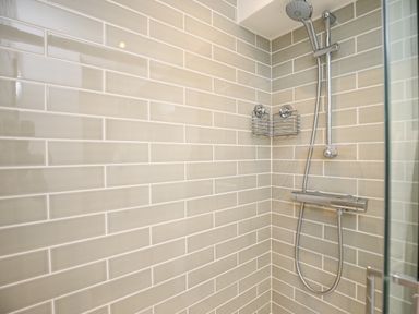 A shower area with beige rectangular tiles and a chrome showerhead at Washpool in Milton-Under-Wychwood