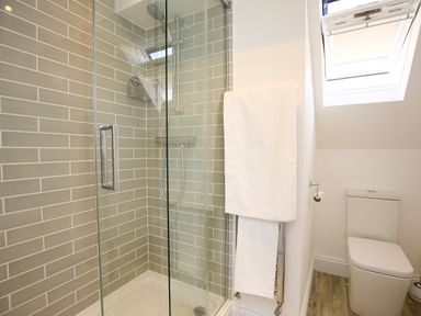 A bathroom with a glass shower enclosure tiled walls a towel rack with towels a toilet and a window at Washpool in Milton-Under-Wychwood