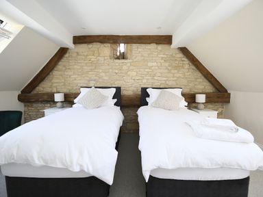 A bedroom with two single beds white bedding a stone wall and wooden beams at Washpool in Milton-Under-Wychwood