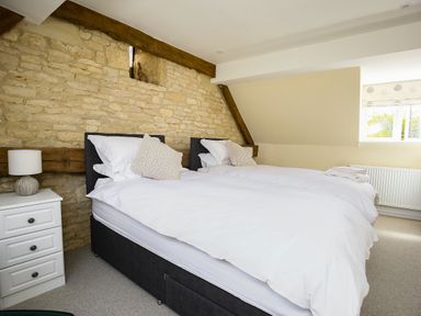 A bedroom with two single beds a nightstand with a lamp and a window at Washpool in Milton-Under-Wychwood
