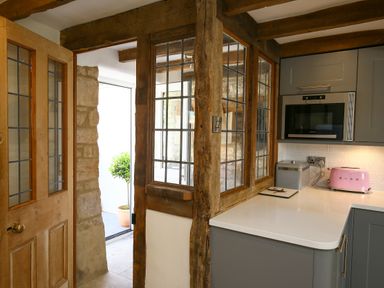 A kitchen with a wooden door stone wall window with wooden beams microwave pink toaster and container on countertop at Washpool in Milton-Under-Wychwood