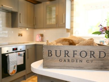A kitchen with grey cabinets and a wooden crate on a white countertop at Washpool in Milton-Under-Wychwood