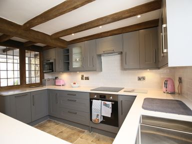 A kitchen with gray cabinets wooden beams white countertops a pink toaster a pink kettle and built in oven at Washpool in Milton-Under-Wychwood