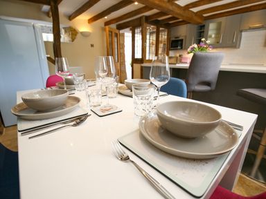 A dining table set with bowls plates glasses and cutlery in a kitchen with wooden beams at Washpool in Milton-Under-Wychwood