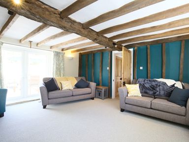 A living room with two sofas pillows exposed wooden beams and a wooden door at Washpool in Milton-Under-Wychwood