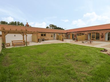An outdoor courtyard with grass lawn wooden pergola seating and brick buildings at Plough Cottage in Little Kelk near Bridlington