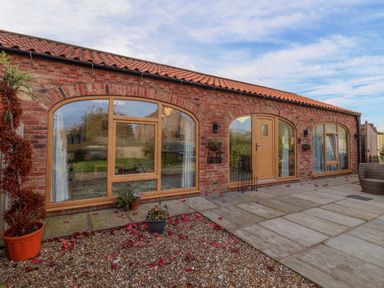 A brick exterior with three large arched windows and a wooden door at Plough Cottage in Little Kelk near Bridlington