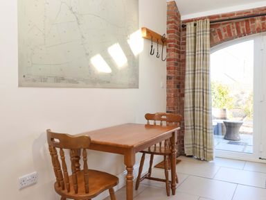 A small dining area with a wooden table and two chairs near a brick arch window with plaid curtains at Plough Cottage Little Kelk near Bridlington