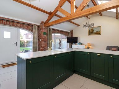 A kitchen with green cabinets white countertops wooden beams and a brick wall at Plough Cottage Little Kelk near Bridlington