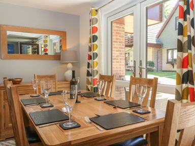 A dining room with a wooden table set with placemats glasses and cutlery near a window with patterned curtains at 32 Trevithick in Hayle