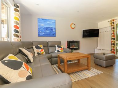 A living room with a gray sectional sofa with patterned cushions a wooden coffee table a wall-mounted television and a fireplace at 32 Trevithick in Hayle