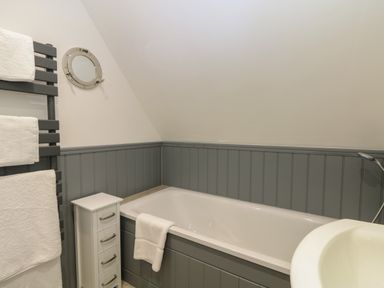 A bathroom with a bathtub a white towel on the bathtub a small cabinet and a towel rail with white towels at 32 Trevithick in Hayle