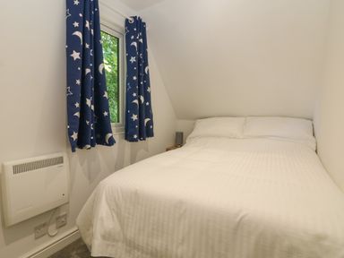 A bedroom with a bed with white bedding and blue curtains with moon and star patterns at 32 Trevithick in Hayle