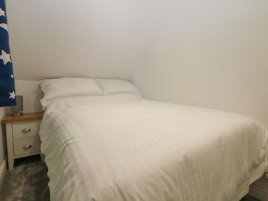 A bedroom with a bed white bedding and a nightstand with a lamp at 32 Trevithick in Hayle