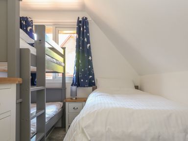 A bedroom with a bunk bed a single bed and a window with blue curtains at 32 Trevithick in Hayle