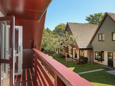 A balcony with red railing overlooking houses with sloped roofs and a lawn at 32 Trevithick in Hayle