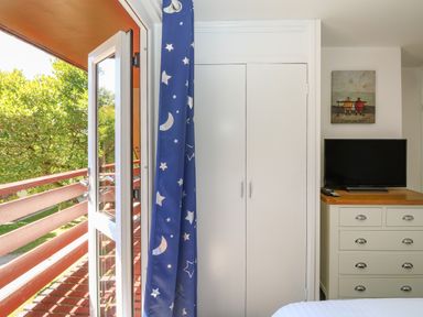 A bedroom corner with a balcony door, blue curtain with moon and stars, white closet, TV on a dresser, and wall art at 32 Trevithick in Hayle