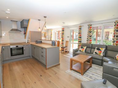 A kitchen with gray cabinets and wooden countertops next to a living area with gray leather sofas and patterned curtains at 32 Trevithick in Hayle