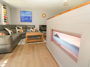 A living room with a gray sectional sofa and patterned cushions a wooden coffee table a blue painting a clock and a wall-mounted electric fireplace at 32 Trevithick in Hayle
