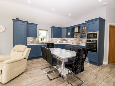 A kitchen with blue cabinets a dining table with black chairs and a beige armchair at Strawberry Stables in Iwood near Congresbury