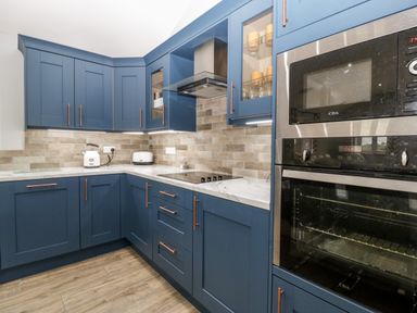 A kitchen with blue cabinets a built-in oven microwave a stovetop toaster kettle and a tiled backsplash at Strawberry Stables in Iwood near Congresbury