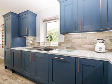 A kitchen with blue cabinets a white countertop a sink under a window and a white kettle on the counter at Strawberry Stables in Iwood near Congresbury